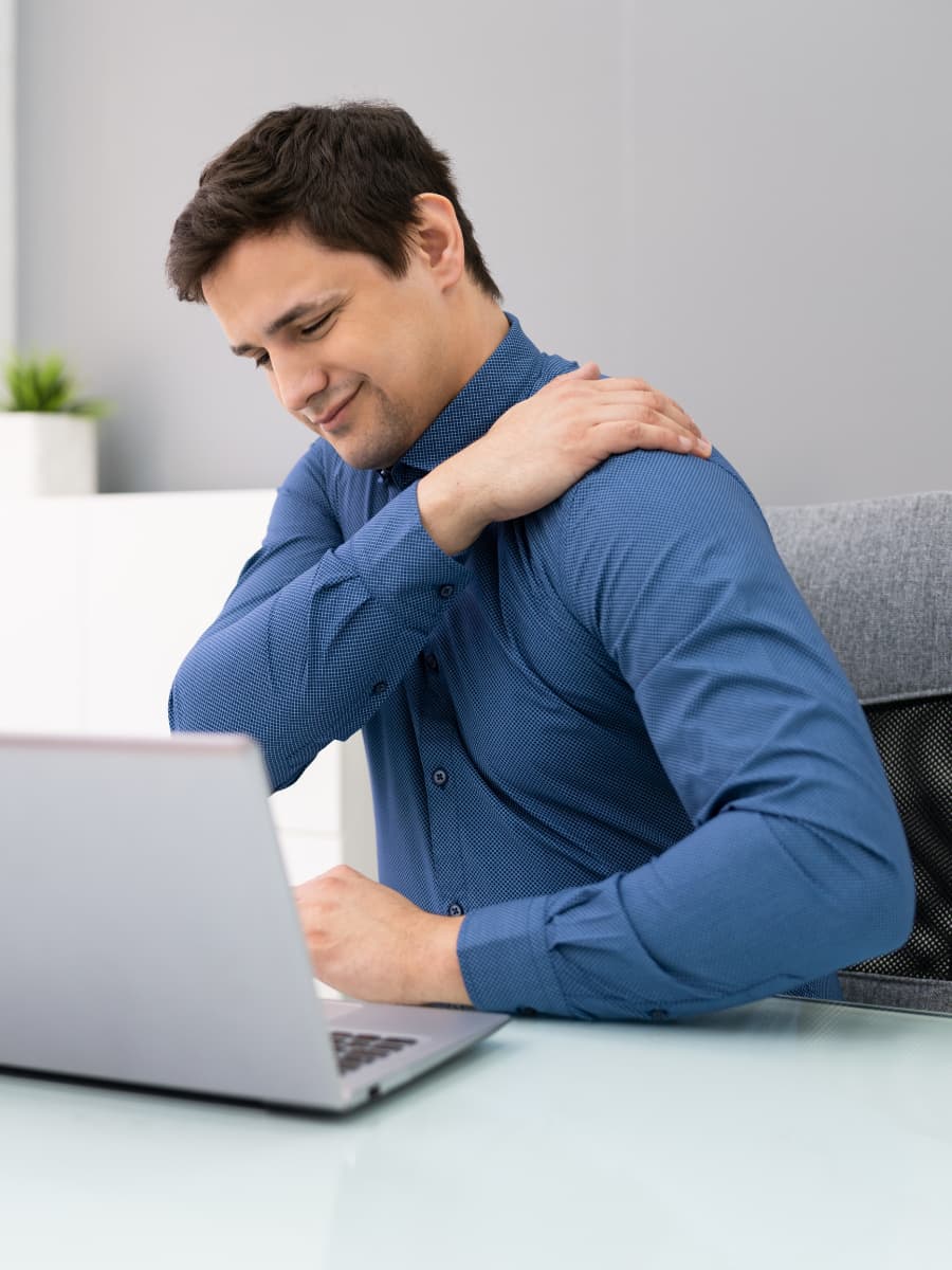 Office worker rubbing their shoulder in front of their laptop